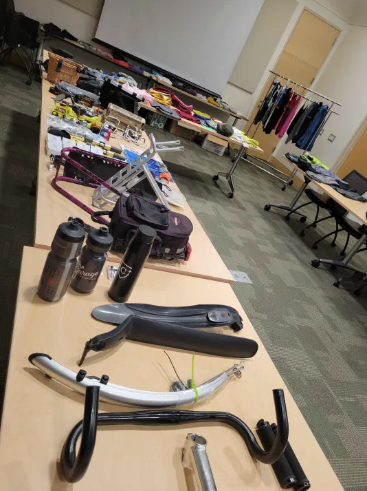 Table with various bike parts, water bottles, bike accessories, and clothing.