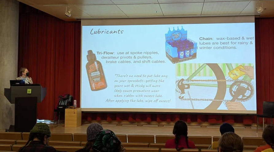 Stage with person presenting. Slide shows description of different kinds of chain lubricants.