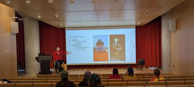 Stage with person presenting. Slide shows a person wearing warm winter gear and bright lights.