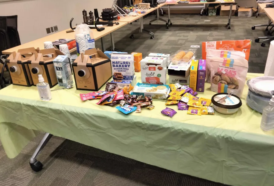 Snack table with coffee, granola bars, hummus, fruit snacks, pita, and more.